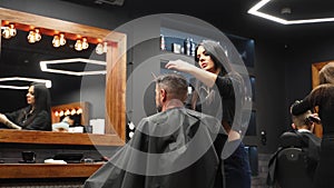 Attractive barber girl cutting man`s hair with scissors and comb. Female hair cutter working serving client. Stylish man