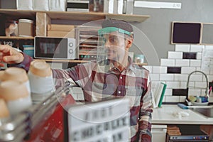 Attractive barista in protective visor standing near coffee machine taking cup