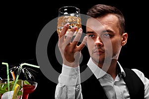 An attractive bartender holds a glass of whiskey, margarita glasses on a bar counter on a black background.