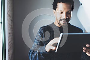 Attractive bearded African businessman using tablet while standing at his modern home office.Concept of young people