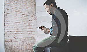 Attractive bearded African man using tablet while sitting on the sofa at his modern home office.Concept of young people
