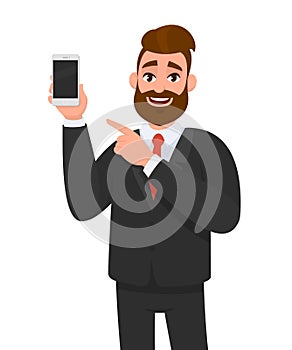 Attractive bearded businessman holding/showing brand new smartphone/mobile/cell phone in hand and pointing index finger towards.