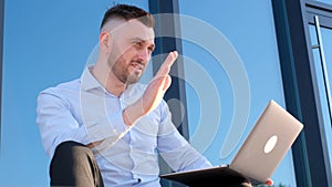 An attractive bearded man in a blue shirt is chatting on the Internet on an iPod outside