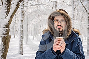 Attractive bearded man in eyeglasses posing outdoor in the cold of winter. Winter street portrait. Coffee or tea in a