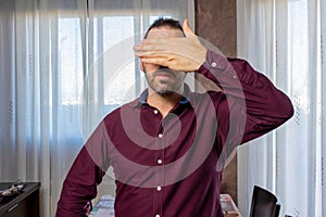 Attractive bearded man in a purple shirt with one hand covering his face