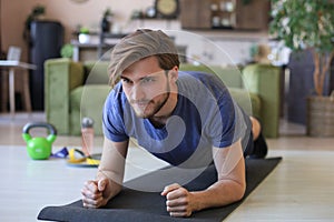 Attractive beared man doing plank exercise at home during quarantine. Fitness is the key to health