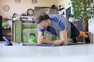 Attractive beared man doing plank exercise at home during quarantine. Fitness is the key to health