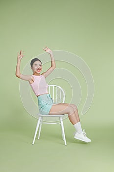 Attractive beautiful Asian woman sitting on white modern chair and hands up raised arms from happiness