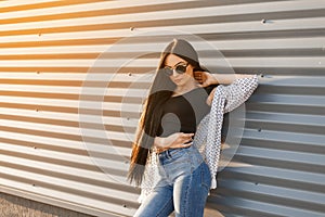 Attractive beautiful hipster woman with long hair in vintage round glasses in stylish summer clothes poses