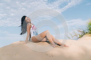 Attractive beautiful young girl having fun on the beach, posing lying on the sand, view from below, smiling broadly and