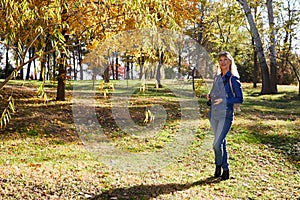 Attractive beautiful young girl holding modern mirror camera in autumn park. Traveller walking in place with yellow leaves on tree