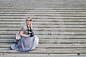 Attractive beautiful young girl holding modern mirror camera on the steps of stair. Female traveller in old place