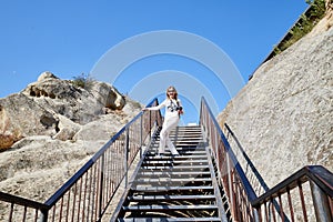 Attractive beautiful young girl holding modern mirror camera on the steps of stair. Female traveller in old place