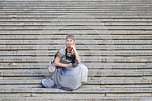 Attractive beautiful young girl holding modern mirror camera on the steps of stair. Female traveller in old place