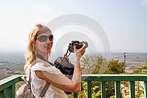 Attractive beautiful young girl who is female photographer traveller holding modern mirror camera in the hands outdoors in the
