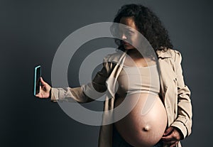 Attractive beautiful young gravid female, expectant mother photographing her tummy in third trimester of happy pregnancy