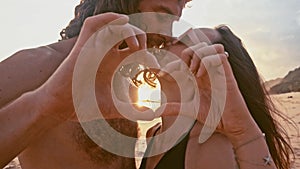 Attractive beautiful young travel couple enjoying sunset on the beach, kissing, holding hands and making a heart shape