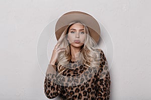 Attractive beautiful young woman in an elegant beige hat in a trendy leopard sweater with curly blond hair