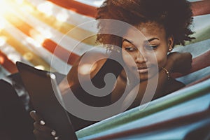 Attractive black cirly girl with digital tablet in hammock