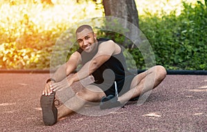 Attractive black guy stretching his legs on asphalt road at park