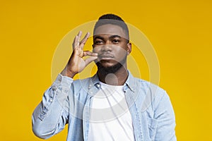 Attractive black man zipping his mouth shut on yellow background