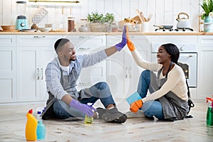 Attractive black woman giving high five to her boyfriend after house cleanup, sitting on kitchen floor, having rest