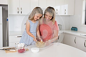 attractive blond 30s woman cooking and baking happy together with sweet adorable mini chef little girl at home modern kitchen