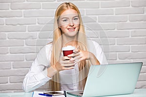 Attractive blond business woman working on her laptop and drinking coffee in her office