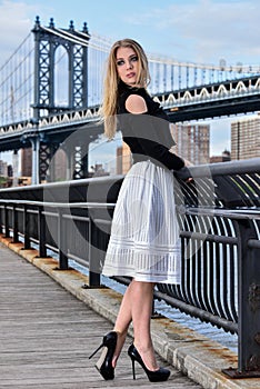 Attractive blond fashion model posing pretty on the pier with Manhattan Bridge on the background.