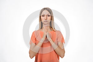 Attractive blond girl prays for wellness of family, keeps palms pressed together in praying gesture