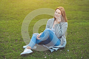 Attractive blond girl talking on mobile phone sitting on grass