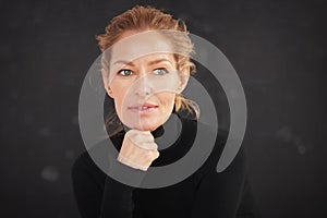 Attractive blond haired woman wearing roll neck sweater and thinking while sitting at dark background