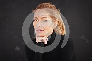 Attractive blond haired woman wearing roll neck sweater and thinking while sitting at dark background