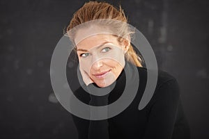 Attractive blond haired woman wearing roll neck sweater and thinking while sitting at dark background