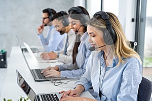 Attractive blond haired young woman working in a call center with group of her colleagues.