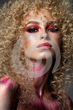 Attractive blond model with a very volume curl hairstyle, colorful red smoky eyes and elements of body art
