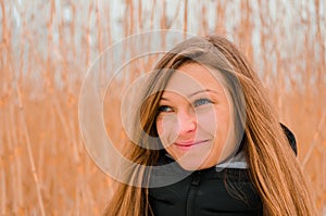 Attractive blond woman cute smiles on a background of dry grass in winter