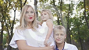 Attractive blond woman holding baby daughter in her arms while older son hugging mother smiling. Portrait of happy