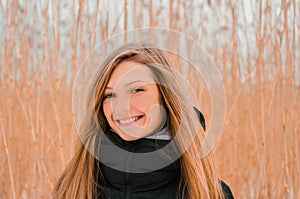 Attractive blond woman widely smiles against a background of dry grass in winter