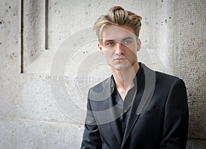 Attractive blond young man in jacket, against a wall photo
