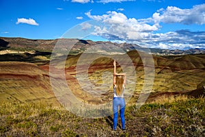 Attractive blond young woman is impressed by the view of the Painted Hills Unit - John Day Fossil Beds National Monument, Oregon,