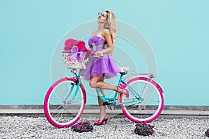 Attractive blonde beauty on colorful bike, decorated with flowers. Spring concept. Beautiful natural woman in elegant pastel dress