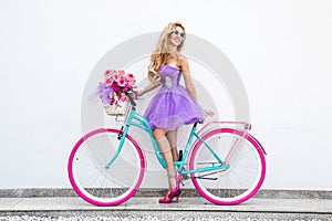 Attractive blonde beauty on colorful bike, decorated with flowers. Spring concept. Beautiful natural woman in elegant pastel dress