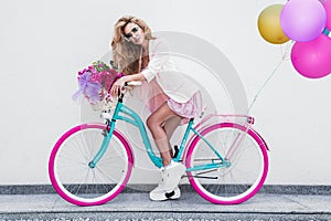 Attractive blonde beauty on decorated bike with flowers and balloons. Spring concept. Beautiful natural woman in colorful, pastel