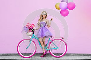 Attractive blonde beauty on decorated bike with flowers and balloons. Spring concept. Beautiful natural woman in colorful, pastel
