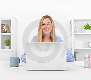 Attractive blonde in a blue business suit in a bright office working on a laptop.