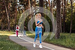 Attractive blonde caucasian woman with sexy body in fashion sports blue clothes jogging in public park in sunny day. Girl running