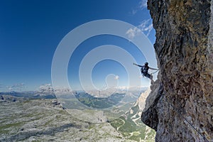 Attractive blonde female climber on a steep Via Ferrata pointing to the sky