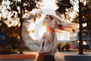 Attractive blonde girl in striped shirt smiling at sunset. Happy dancing Hipster lifestyle