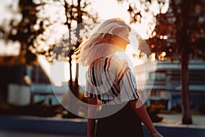 Attractive blonde girl in striped shirt smiling at sunset. Happy dancing Hipster lifestyle